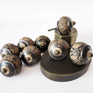 May include: A set of eight decorative cabinet knobs with a black and brown patterned design. The knobs have a gold-colored metal accent in the center.