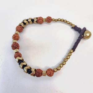Könnte beinhalten: Ein braunes und goldenes Perlenarmband mit einem dunkelgrauen Band und einer goldenen Metallperle am Ende.
