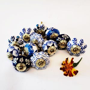 Może przedstawiać: Zbiór ceramicznych gałek w kolorze niebieskim i białym z kwiatowymi wzorami. Gałki mają złoty akcent wokół środka.