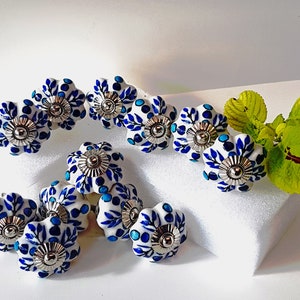 Könnte beinhalten: Ein Satz von zehn blauen und weißen Keramik-Schubladengriffen mit floralem Design. Jeder Griff hat einen silbernen Metallakzent in der Mitte.