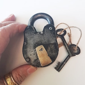 May include: A black metal padlock with a brass keyhole and a brass key attached to a twine string. The padlock has a worn, aged look.