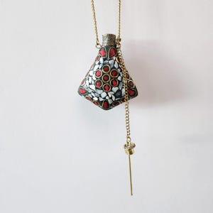 May include: A gold chain necklace with a geometric, black, white and red mosaic pendant. The pendant is a small bottle with a stopper on a chain.