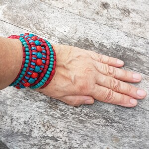 May include: A stack of colorful wooden bead bracelets in shades of red and turquoise. The bracelets are worn on a person's wrist.