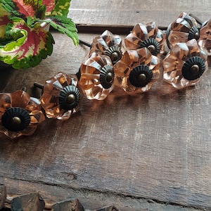 May include: A set of eight pink glass cabinet knobs with a decorative floral design and a metal accent.