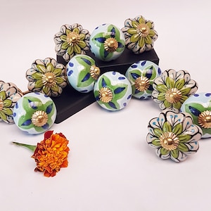 May include: A collection of 12 ceramic knobs with green, blue, and white floral designs. The knobs have a gold accent in the center.