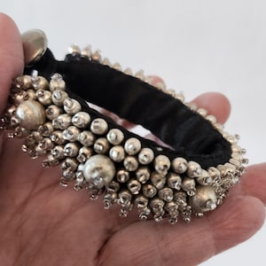 May include: A silver beaded bracelet with a black fabric backing. The beads are clustered together in a dense pattern.