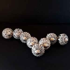 Könnte beinhalten: Ein Satz von acht weißen Keramik-Schubladengriffen mit schwarzen Blumenmustern. Jeder Griff hat einen silbernen Metallakzent in der Mitte.