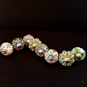 May include: A set of eight ceramic drawer knobs with colourful floral patterns. The knobs are round and have a silver metal base.