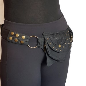 May include: A black fabric belt with a large, round metal ring and a small black pouch with a zipper and lace trim. The pouch is decorated with gold-coloured metal studs.