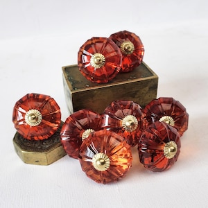 May include: Eight amber glass cabinet knobs with gold accents. The knobs have a faceted design and are arranged on a wooden surface.