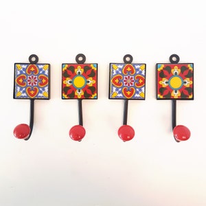 Könnte beinhalten: Set aus vier dekorativen Wandhaken mit roten, gelben, blauen und grünen Fliesenmustern. Jeder Haken hat eine schwarze Metallbasis und einen roten Knopf.