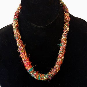 May include: A colorful, multi-strand necklace made of woven fabric and gold thread. The necklace is thick and has a chunky, textured look.