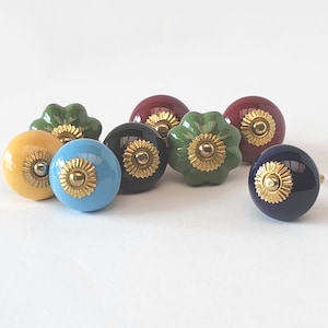 May include: Assortment of ceramic cabinet knobs in various colors, including yellow, blue, green, red, black, and navy blue. Each knob features a gold-colored center detail.