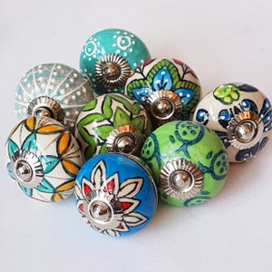 May include: Assortment of 10 colorful ceramic cabinet knobs with floral and geometric patterns. The knobs are in shades of blue, green, white, and yellow.