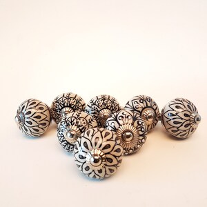 May include: A set of eight ceramic drawer knobs with a white background and black floral designs. The knobs have a silver finish.