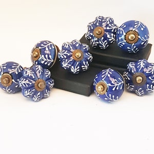 May include: A selection of blue ceramic door knobs featuring white leaf patterns and brass fittings. The knobs, in round and floral shapes, are displayed on a white surface. Each knob is approximately 4 cm in diameter.