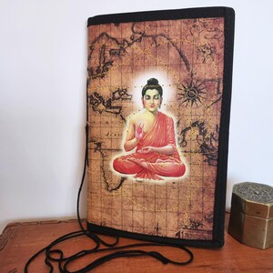 May include: A rectangular journal cover featuring a seated Buddha image in red and gold, set against a vintage map background. The cover has a black border and a black cord for closure. The design includes gold stitching.