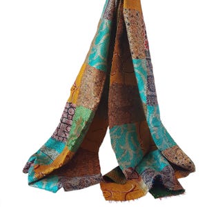 May include: A long, patchwork scarf made of silk in shades of turquoise, brown, yellow, and green. The scarf is made of several different pieces of fabric sewn together, creating a unique and colorful design.