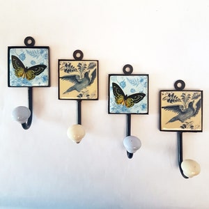 May include: Four decorative wall hooks with ceramic tile accents. Each hook features a different design with a bird and butterfly motif. The tiles are in shades of blue, yellow, and white.