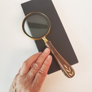 May include: A magnifying glass with a gold rim and a brown wooden handle with a carved leaf design.