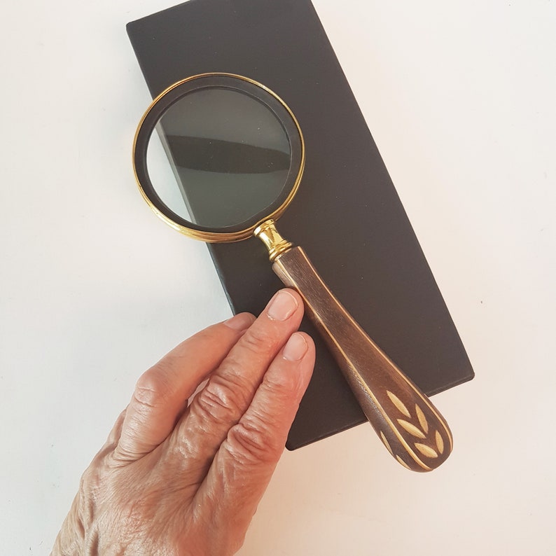 May include: A magnifying glass with a gold rim and a brown wooden handle with a carved leaf design.