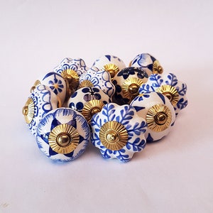 Peut inclure: Un ensemble de 14 boutons en céramique bleu et blanc avec des accents dorés. Les boutons présentent différents motifs floraux et géométriques.