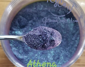 May include: A close-up of a jar of purple and blue iridescent glitter with a spoonful of glitter in the foreground. The jar is labeled "Athena" and "GlitterandCraftsU.com".