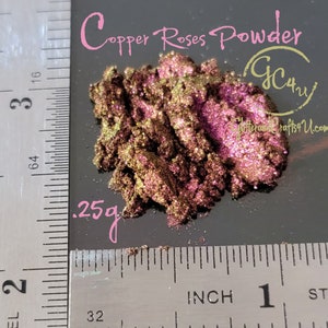 May include: A close-up of a small pile of copper rose powder, a shimmery, iridescent pigment with a golden and pink hue. The powder is measured out on a ruler, showing a quantity of 0.25 grams.