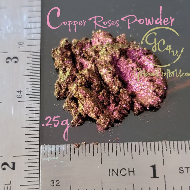 May include: A close-up of a small pile of copper rose powder, a shimmery, iridescent pigment with a golden and pink hue. The powder is measured out on a ruler, showing a quantity of 0.25 grams.