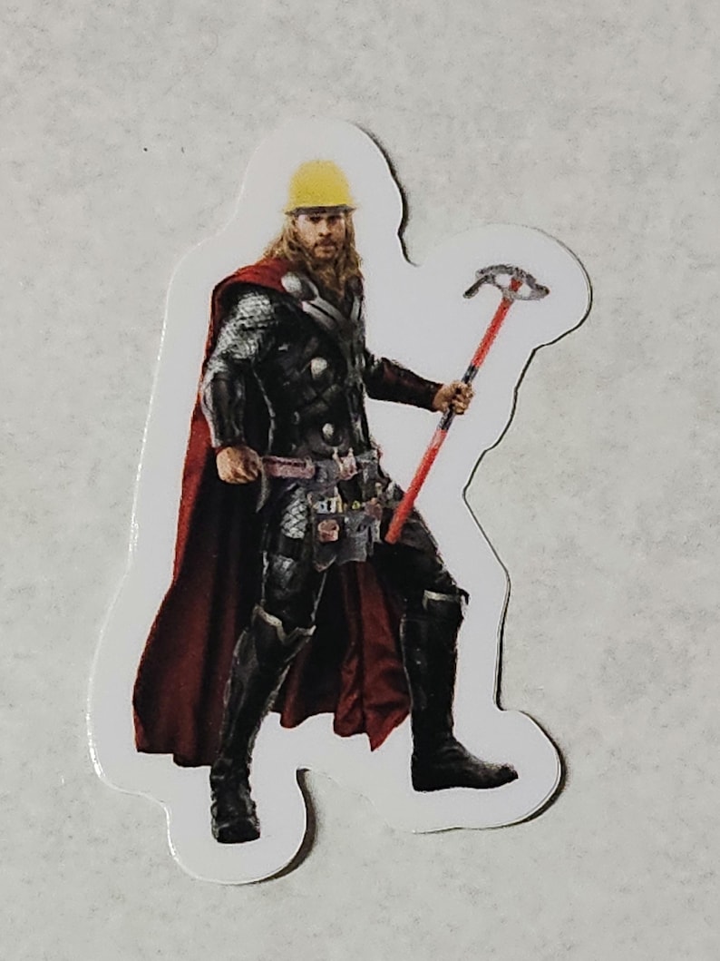 Pode incluir: Um adesivo com um super-her&oacute;i usando um capacete amarelo e uma capa vermelha, segurando uma ferramenta vermelha e prateada.