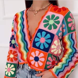 May include: A colorful crochet cardigan with a rainbow pattern and floral motifs. The cardigan has a V-neck and long sleeves.