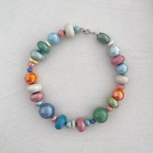 Puede incluir: Un collar de cuentas de cer&aacute;mica de colores con un cierre plateado. Las cuentas son en tonos de azul, verde, naranja, rosa y blanco.