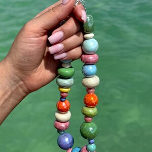 Puede incluir: Un collar de cuentas de cer&aacute;mica de colores con una variedad de colores, incluyendo verde, azul, rosa, naranja y amarillo. Las cuentas son redondas y tienen un acabado brillante.