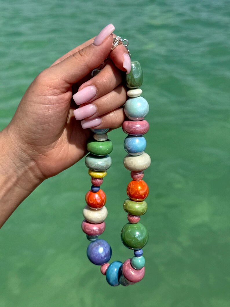 Puede incluir: Un collar de cuentas de cer&aacute;mica de colores con una variedad de colores, incluyendo verde, azul, rosa, naranja y amarillo. Las cuentas son redondas y tienen un acabado brillante.