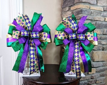 May include: Two Mardi Gras themed bows with gold, green, and purple ribbon and glitter. The bows are displayed on a small wooden table.