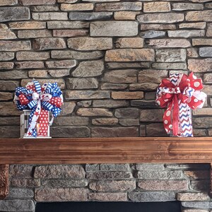 May include: Two red, white and blue patriotic bows with white polka dots and stars on a stone fireplace mantel.