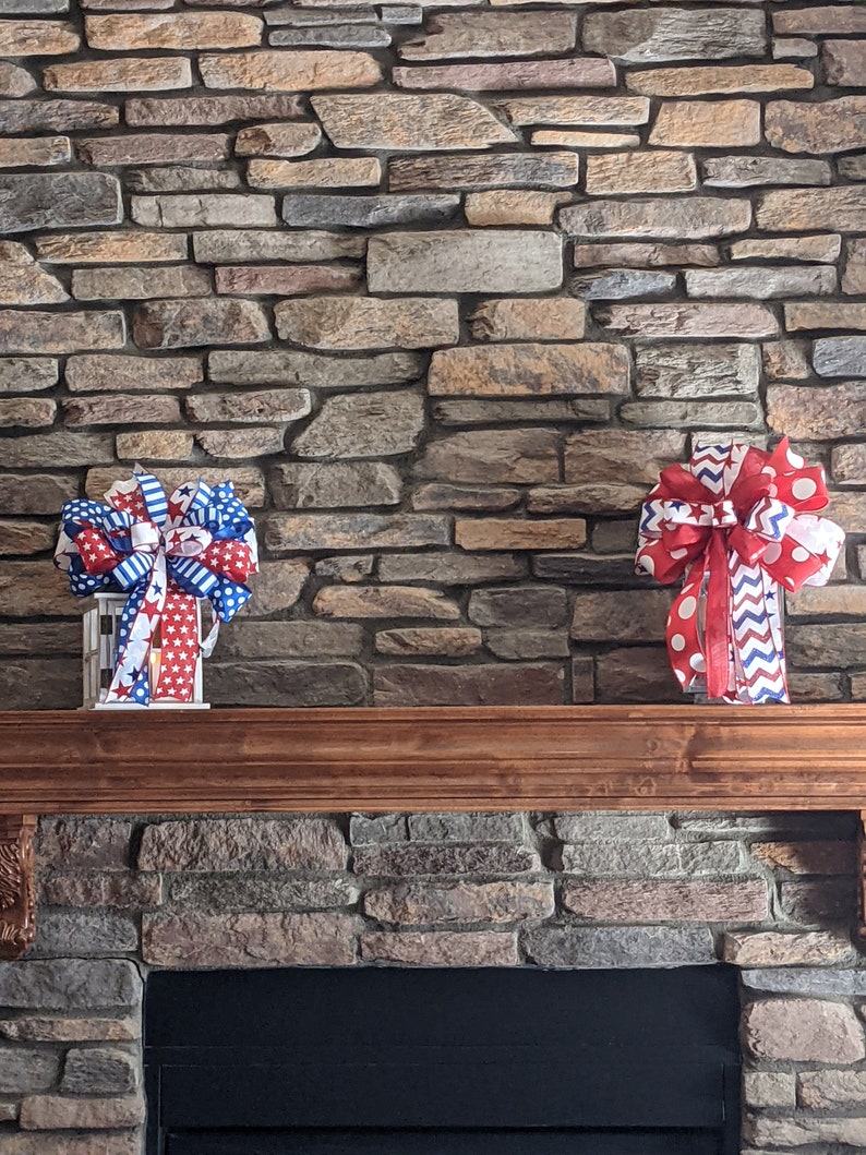 May include: Two red, white and blue patriotic bows with white polka dots and stars on a stone fireplace mantel.