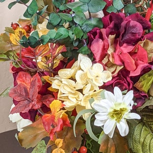 May include: A floral arrangement in a green vase with red, white, and yellow flowers, green leaves, and red berries.