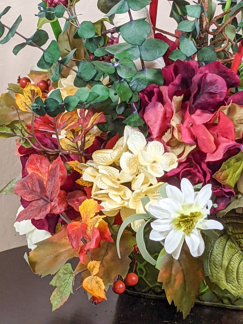 May include: A floral arrangement in a green vase with red, white, and yellow flowers, green leaves, and red berries.
