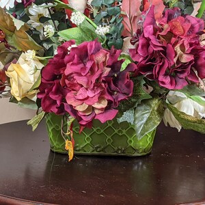 May include: A green ceramic planter with a lattice design holds a floral arrangement featuring pink and white flowers, green leaves, and red berries.