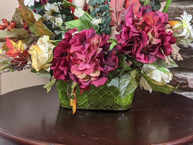 May include: A green ceramic planter with a lattice design holds a floral arrangement featuring pink and white flowers, green leaves, and red berries.