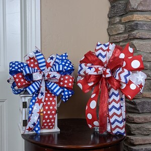 May include: Two red, white and blue ribbon bows with stars and polka dots. The bows are on a wooden table in front of a brick wall.