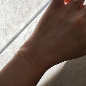 May include: A thin gold chain bracelet on a person's wrist.