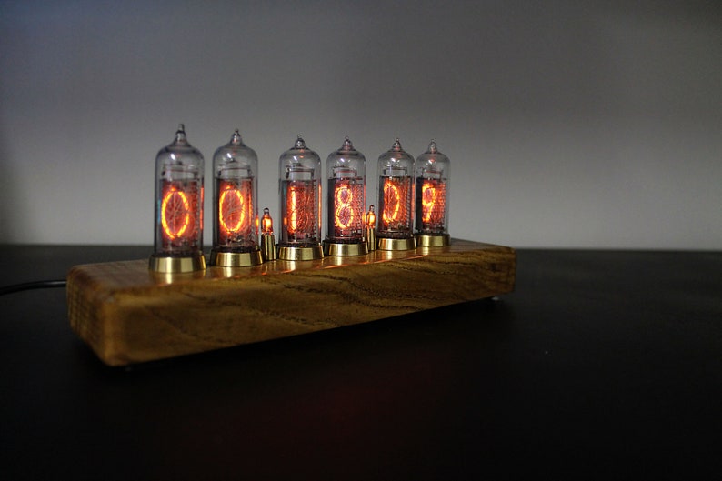 May include: A wooden base with six clear glass Nixie tubes displaying the time as "00:18:09". The tubes are lit with an orange glow.