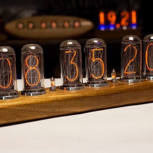 Puede incluir: Un reloj de madera con cinco tubos Nixie naranjas brillantes que muestran la hora 08:35:20. El reloj est&aacute; hecho de madera oscura y tiene un dise&ntilde;o elegante y moderno.