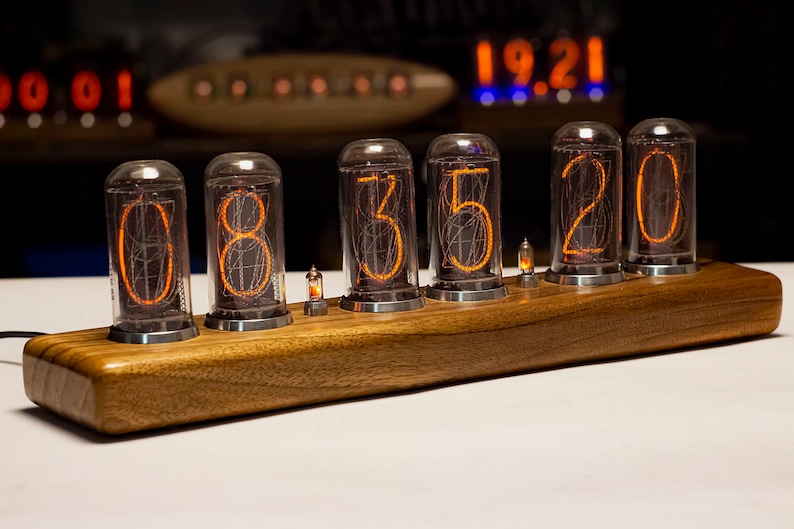 Puede incluir: Un reloj de madera con cinco tubos Nixie naranjas brillantes que muestran la hora 08:35:20. El reloj est&aacute; hecho de madera oscura y tiene un dise&ntilde;o elegante y moderno.