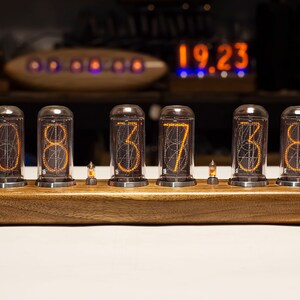 Puede incluir: Un reloj de madera con seis tubos Nixie naranjas que muestran la hora 08:37:38. El reloj est&aacute; sobre una superficie blanca.
