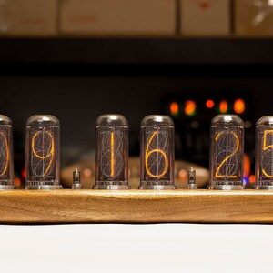 Puede incluir: Un reloj de madera con seis tubos Nixie naranjas brillantes que muestran la hora 09:16:25.