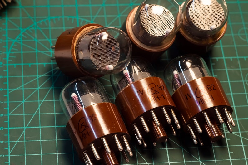 May include: Close-up of six brown glass vacuum tubes with metal pins. The tubes have a clear glass section with a wire mesh inside. The tubes are labeled "IV 282 H-1".