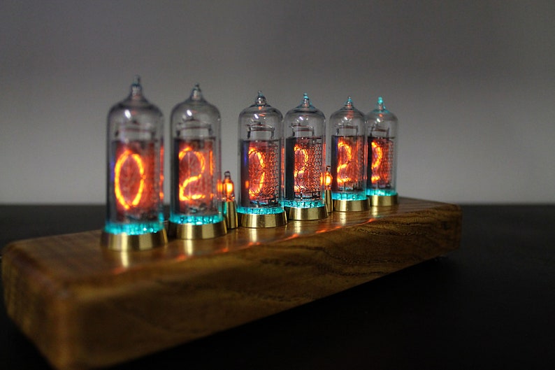 May include: A wooden clock with six glowing orange Nixie tubes displaying the time "02:22:22". The tubes are encased in glass and have a blue glow around the base.